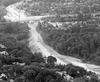 A black and white photo taken from the air, showing the progress on a road under construction through a forested valley