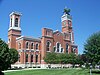 A brick courthouse sits on a grass lawn with a tree growing on the steeple.