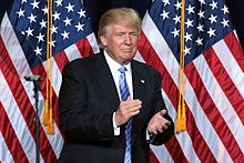 President Donald Trump clapping in front of U.S. flags