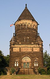 Monument de style gothique en pierre marron. Le premier étage est carré et est surmonté d'un second étage cylindrique et d'un toit conique.