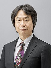 Shigeru Miyamoto, a middle-aged Japanese man wearing a herringbone blazer and white shirt.