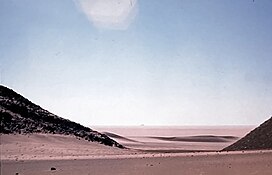 "Adrar Bous in the modern day." A desert landscape with a bright blue sky.