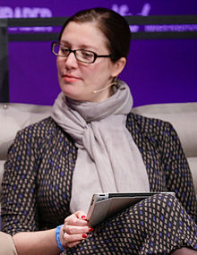 Anita Zielina ist auf einer Fotografie zu sehen. Sie sitzt bei der Veranstaltung NEXT Berlin (2014) auf einem Sofa und hält ein Tablet. Sie trägt Brille und hat dunkle Haare.