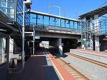 Railway station with two red brick side platforms and a wide concrete bridge, with stairs and lifts linking the platforms to the bridge