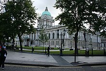 a photograph of part of Donegall Square showing Belfast City Hall viewed through trees lining a pavement with people walking