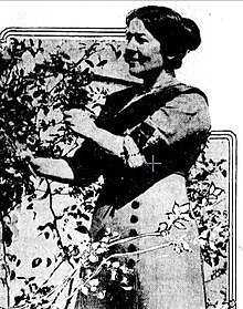 A young white woman standing outdoors, amidst foliage.