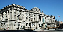 An ornate stone building stretching an entire city block. Architectural features include a dome in the center of the roof, columns along the front of the façade, and two sculpted eagles on the roof.