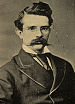 Head and shoulders of an older white man with a bushy beard wearing a suit coat, vest, and bow tie.