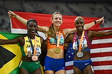 Photo of Rushell Clayton, Femke Bol, and Shamier Little posing with medals around their necks while holding their countries' flags
