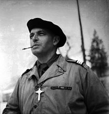 Photographie en noir et blanc d'un homme en uniforme portant un béret et fumant une cigarette.