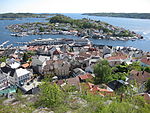 Foto von einem Hang herab auf eine Stadt, die an einem Fjord liegt. Ein Teil der Stadt liegt auf einer durch einen schmalen Sund abgetrennten Insel.