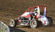 A midget car being driven on a dirt race track.