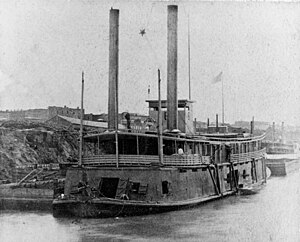 USS Cricket (1863-1865, "Tinclad" # 6) Tied up at a Western Rivers city, during the last years of the Civil War, with a barge astern and a boat alongside. Note the decorative star suspended between her smokestacks.