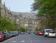 Une grande avenue bordée d'immeubles en pierre grise sur la gauche et d'arbres sur la droite