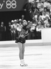 A female figure skater points with her right arm as she performs