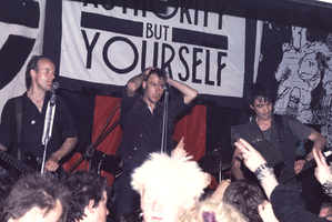 Crass on stage in Cumbria in May 1984, with the slogan "there is no authority but yourself" in the background. From left to right: Pete Wright, Steve Ignorant, and N.A. Palmer.