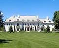 White mansion with four chimneys, trees lining the front, and many windows