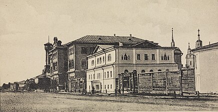 Photographie en noir et blanc d'une rue avec trois bâtiments. Depuis le belvédère de gauche et la tour des pompiers (fond), l'école secondaire pour hommes (centre) et la Douma (vers devant) (1913).