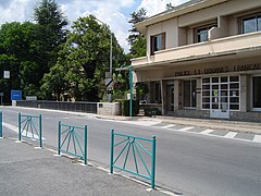 Vue d’un poste de douane, au bord d’une route, bâtiment blanc à un étage.