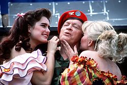 Comedian Bob Hope in the center. Singer Barbara Mandrell is kissing his left cheek, while actress Brooke Shields is stroking his right cheek.