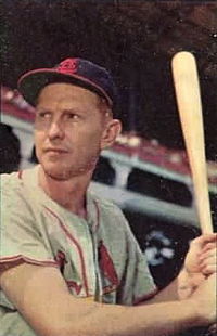 A baseball player in a gray jersey and navy cap stands holding a bat and ready to swing