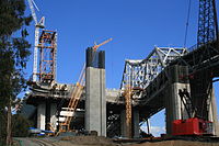 Western end (W2): Western end counterweight, behind (YBITS) approach structure columns, SAS Tower (T1) scaffold/gantry beyond. On the right is the 1936 bridge.
