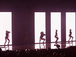 An image showing five women wearing black outfits in front of a screen