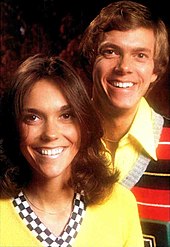 A young woman with long brown hair and a young man with mid-length brown hair, both smiling broadly