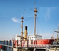 Photograph of Lightship No. 83, Relief, at dock in Seattle as a museum ship, its light masts rising to the sky and its red hull painted with its contemporary name Swiftsure.