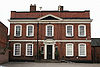 A red-brick building with two storeys, five bays and a central triangular pediment