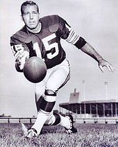 Bart Starr in a Green Bay Packers football uniform poses while underhand tossing a football toward the camera. He is wearing number "15".