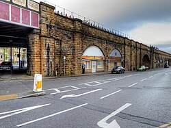 A stone viaduct with a road in the foreground, and businesses occupying the arches of the viaduct