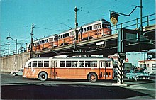 A trolleybus passing under a viaduct on which a train of streetcars is running