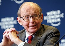 Samuel P. Huntington in a grey suit with a red tie, seated at a desk at the World Economic Forum.