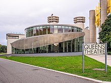 The Queens Theatre, occupying the former Theaterama. The glass structure in the foreground contains the Queens Theatre's entrance, which was added in 2009. Behind the structure is the original Theaterama, a concrete building.