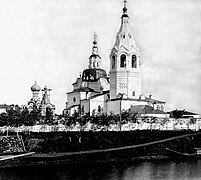 Photographie en contre-plongée de l'église de la Nativité de Ienisseïsk en noir et blanc. L'église est blanche, avec un clocher principal et un clocher secondaire. En arrière-plan, on distingue les coupoles d'une autre église.