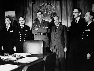 Photo noir et blanc de six hommes dans un bureau ; trois sont en uniforme dont le général De Gaulle.