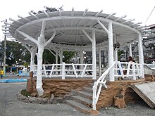 A gazebo that is coated in white paint and a woman sat inside.