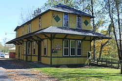 Old but well-refurbished yellow building with black tiling and siding. A sign on the side of the building facing the camera reads "BUCKINGHAM TOWNSHIP MUNICIPAL BUILDING." There is a small post with a map of Wayne County, Pennsylvania attached to it on the same side of the building.