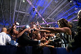 Photograph of Barack and Michelle Obama waving and shaking hands with a crowd of people