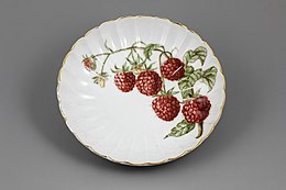 A dessert plate with gilded scalloped edges and a raspberry motif.