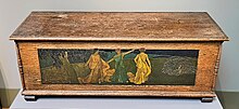 Large wooden chest decorated with a painted carving of three women standing in a landscape.