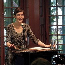 A caucasian woman with short hair lecturing at a podium