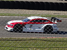 Voiture de course blanche et rouge vue de profil gauche sur une piste goudronnée.