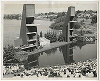 A black and white photograph of a group of performers on a stage in a lake