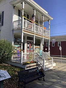 A two-story building with a porch on the first floor, and a balcony with a matching railing on the 2nd floor.