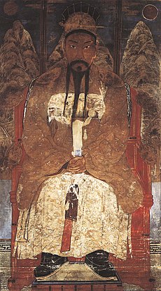 Asian man with mustache and gold robes, sitting down.