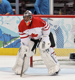 Hockey player in blue Vancouver uniform and goaltender's gear. He is crouched on the ice, legs split far apart.