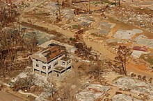 An aerial picture of a destroyed residential neighborhood with only concrete slabs and one home on stilts remaining