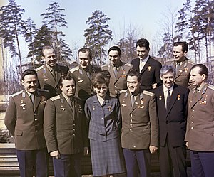 Ten men and one woman standing in two rows, five men behind and higher up than the six at the front. The woman is close to the centre of the front row. Eight of the men are in military uniform consisting of a dark khaki four-button jacket and dark blue trousers; the other three people wear civilian suits. All eleven are wearing the insignia of two awards, one on each breast; those in military uniform wear various additional insignia.